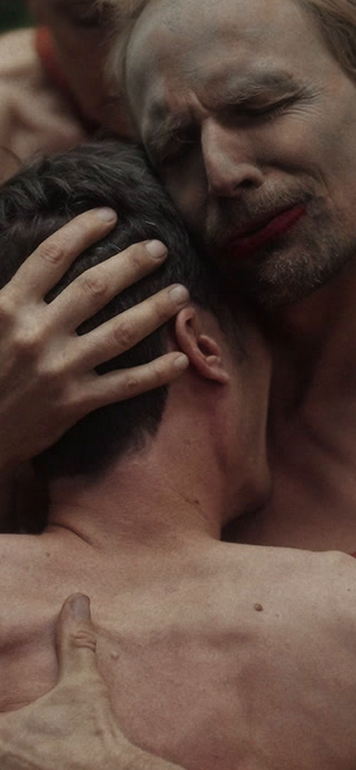 Wolf embracing a man, one hand open on his head and the other resting on his back.