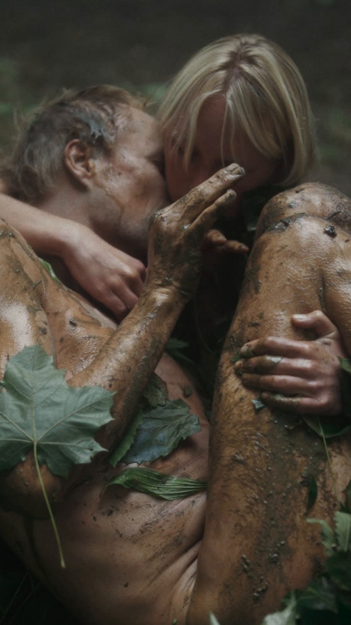 Wolf, covered with earth and leaves, supported in a woman's arms outdoors.